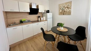 Cocina compacta con armarios blancos, microondas y cafetera. Hay una mesa de comedor con cuatro sillas y una pequeña planta en maceta.