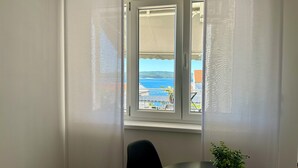 Una habitación con vista al mar, a través de una ventana con cortinas blancas.