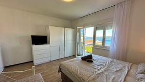 Un dormitorio con cama, televisor en una cómoda, ventana con vistas y balcón.
