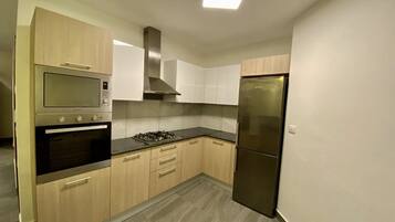 A modern kitchen with built-in appliances, light wood cabinets, and a grey tiled floor.