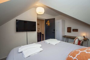 Een hotelkamer met een bed, een aan de muur bevestigde televisie, een deur met het nummer 4 en een bureau met een lamp.