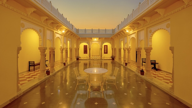 A spacious, well-lit courtyard with a central round table and chairs, surrounded by ornate arches and columns.