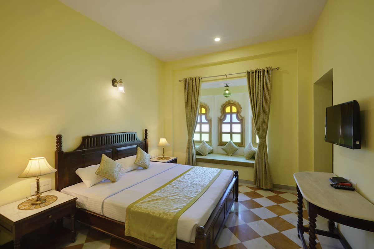Une chambre d’hôtel avec un lit, des tables de chevet, une télévision, une fenêtre avec des rideaux et un sol à carreaux.