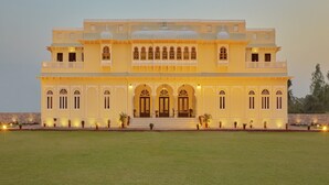 A large, multi-story building with a symmetrical facade, arched windows, and a central entrance with a staircase.