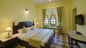 A hotel room with a bed, bedside tables, a TV, a window with curtains, and a checkered floor.