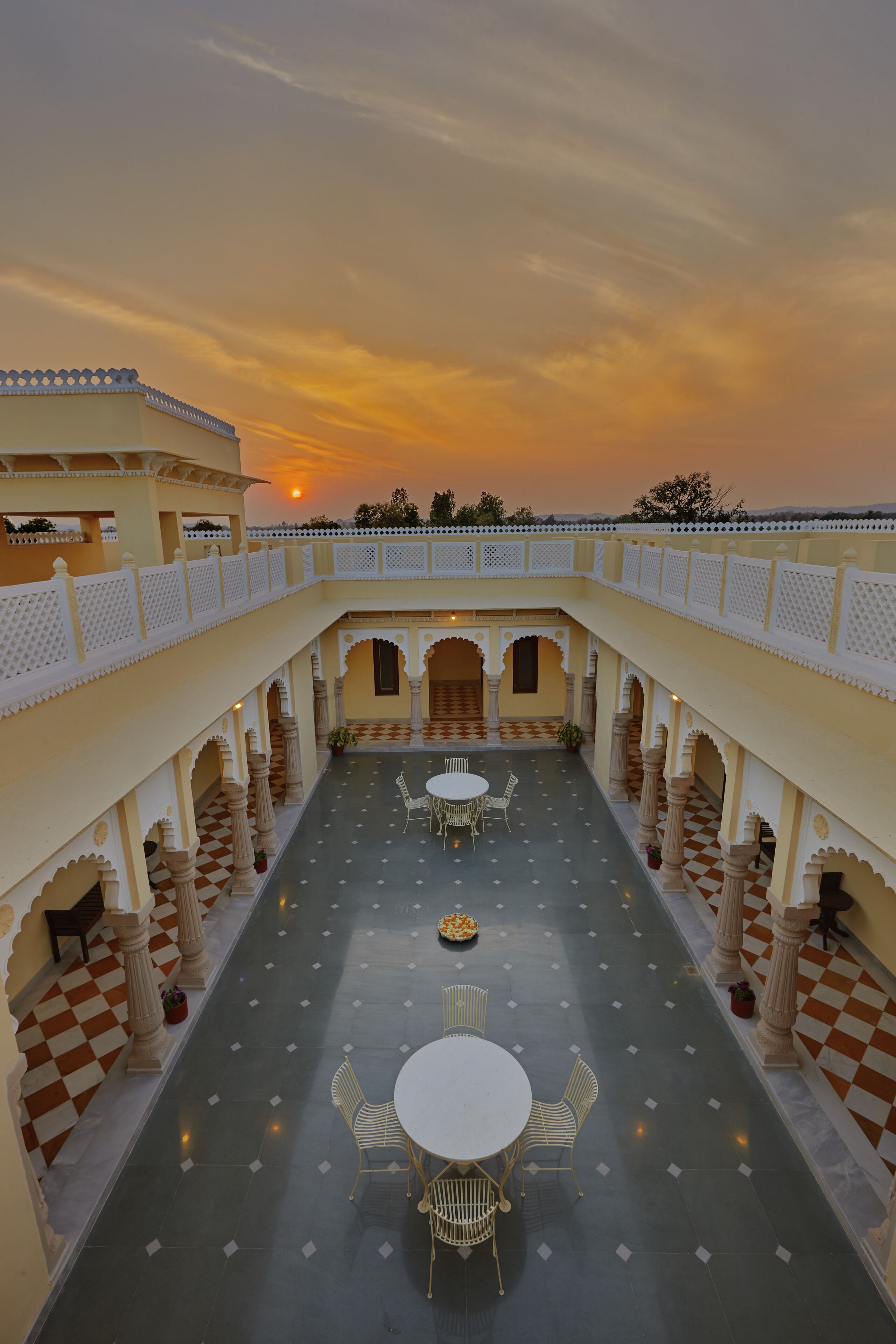 A courtyard with a checkered floor, white columns, and a central seating area with tables and chairs.