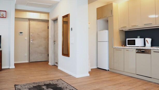 Una cocina moderna con armarios color beige, un microondas y un lavavajillas. Hay piso de madera y un tapete en el pasillo.