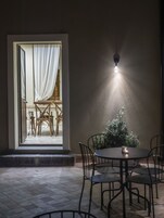 An outdoor patio area with a round table and chairs, a small plant, and a wall-mounted light fixture.