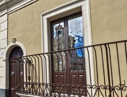 Fachada de edificio con puerta marrón, ventana que refleja una torre y un cartel con el número 29.