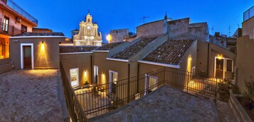 Un patio con una iglesia al fondo, edificios de piedra y una escalera que lleva a un nivel superior.