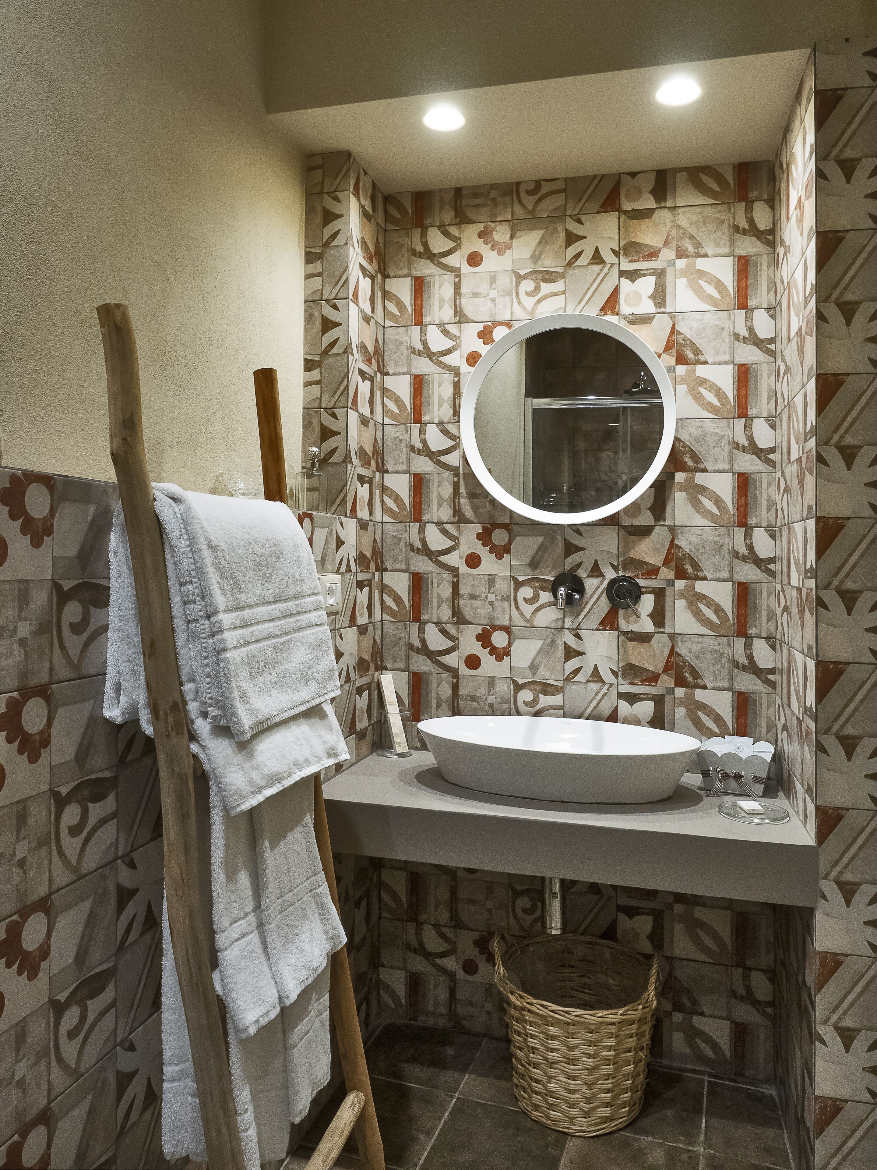 A bathroom with a white sink, a round mirror, and patterned tiles.