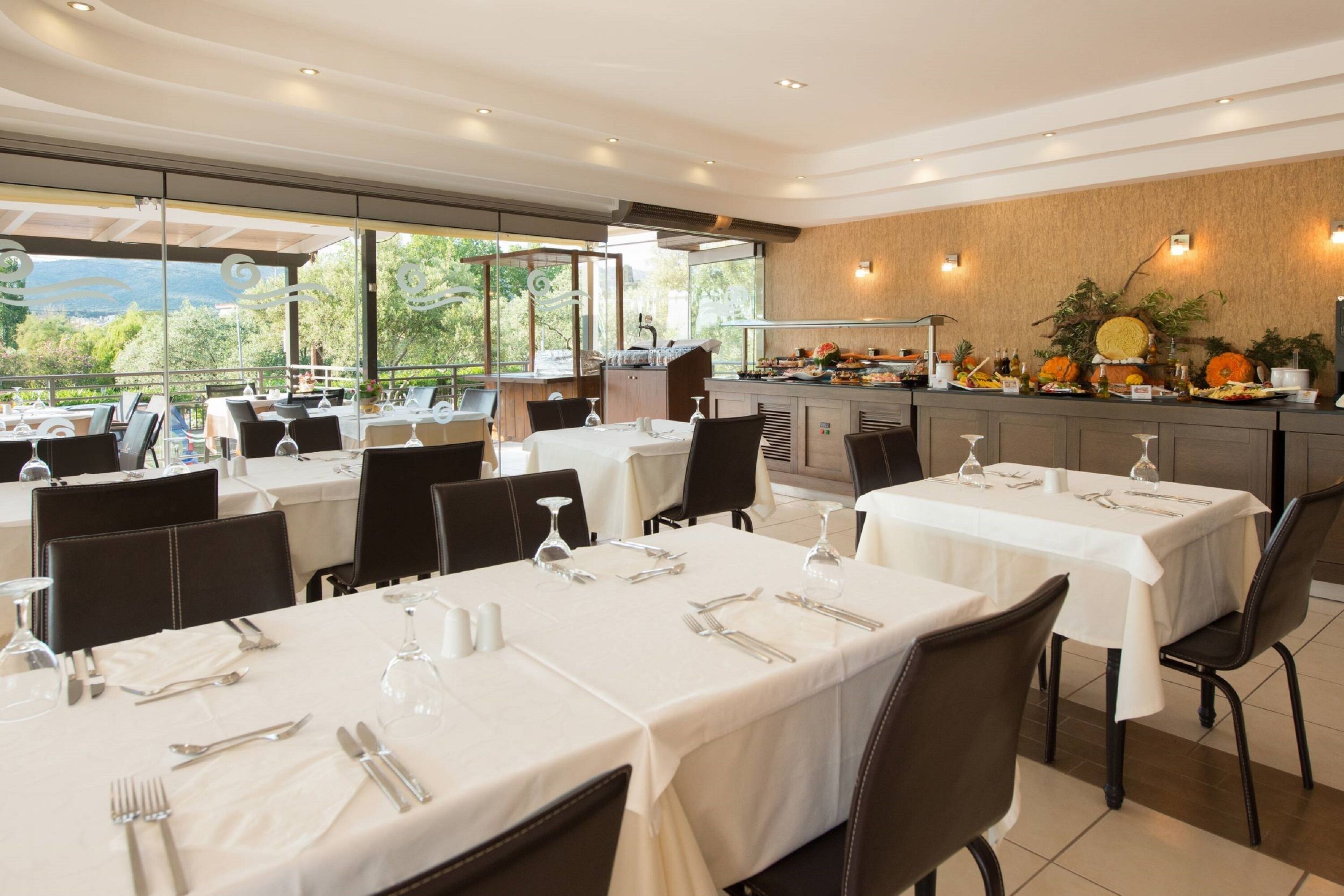 Un restaurant avec des tables dressées pour le service, un espace buffet et une vue sur l’extérieur.
