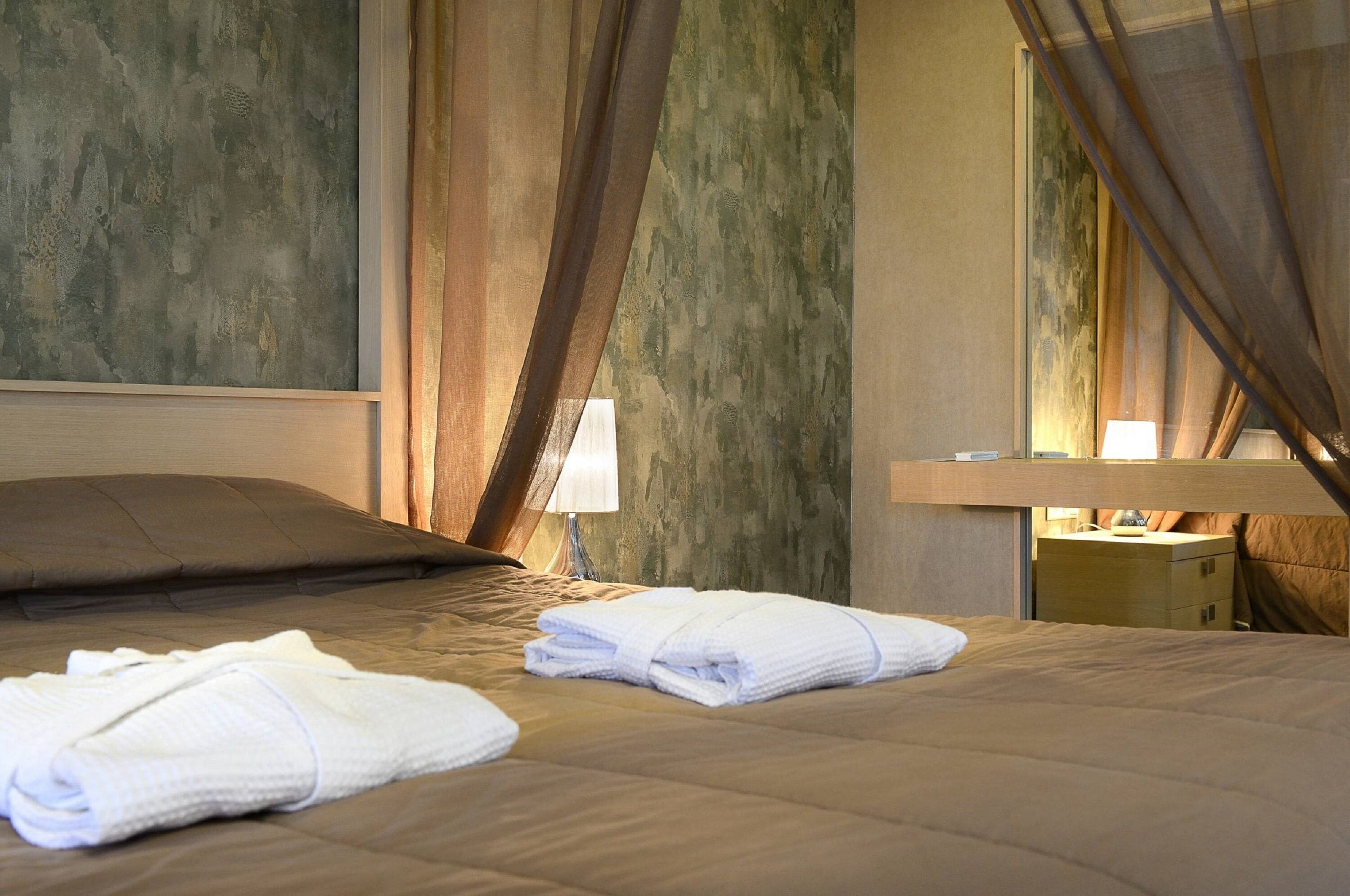 A neatly made bed with white towels, a bedside lamp, and a nightstand with a lamp.