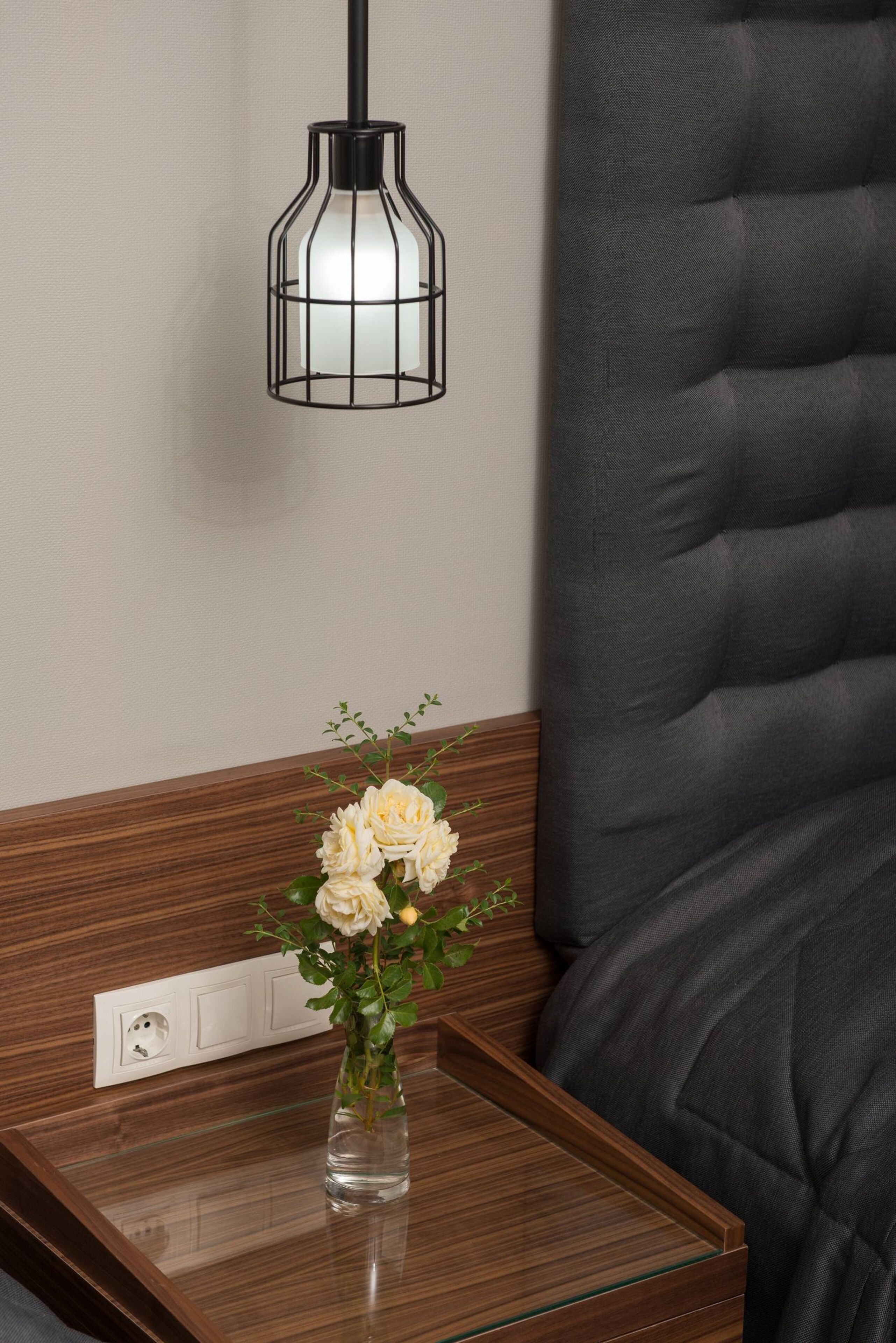 A modern room with a wooden side table, a vase with flowers, and a black pendant light.