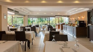 A restaurant with tables set for dining, a bar area, and a view of greenery outside. - Atrium Hotel Thassos by GHH (Thasos)