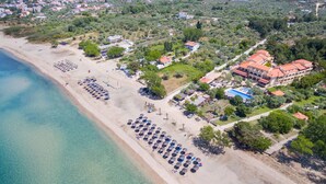 An aerial view of a coastal area with a beach, umbrellas, and buildings. - Atrium Hotel Thassos by GHH (Thasos)