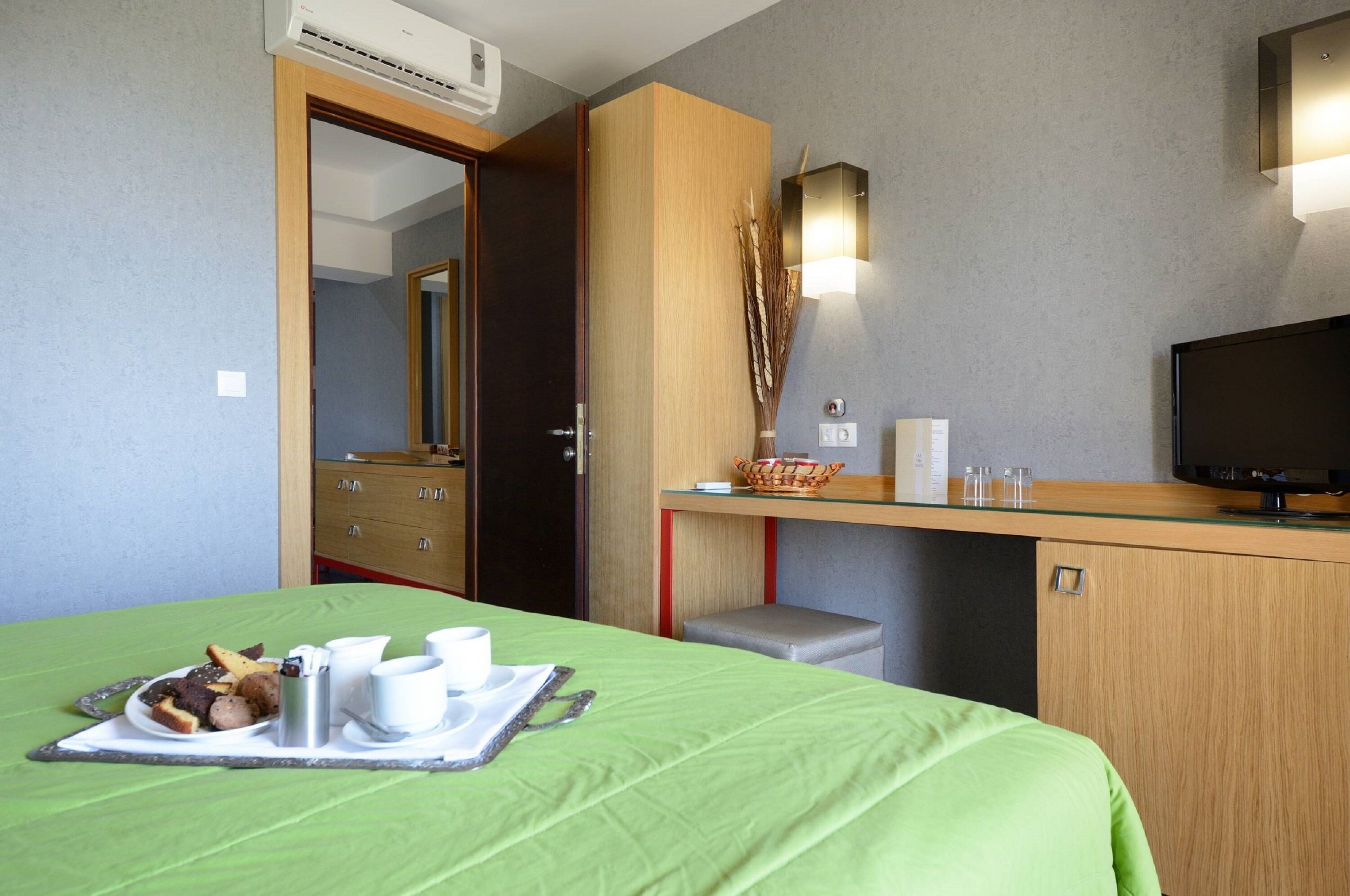A hotel room with a bed, a desk, a television, and a breakfast tray.