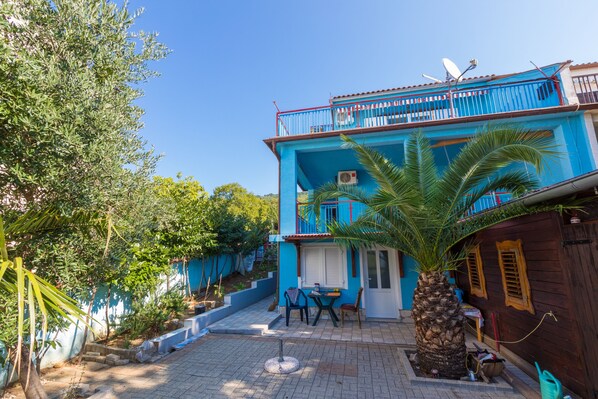 A two-story building with a blue exterior, a balcony with a red railing, and a palm tree in the foreground.