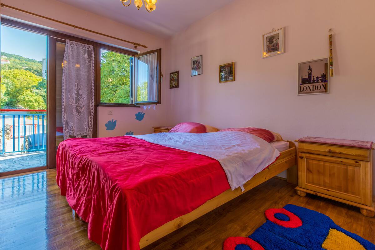 Quarto com cama de madeira, mesa de cabeceira e janela com vista para o verde.