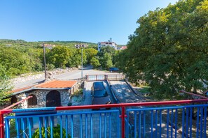 A view from a balcony overlooking a road with a stone building and a parked car.