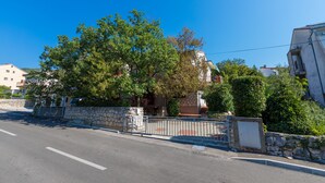 Vista de calle con un muro de piedra, una cerca de metal y un edificio con un árbol grande al frente.