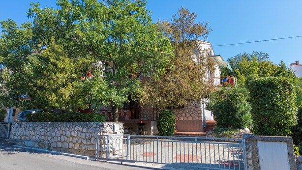 Edificio de paredes de piedra con un balcón, rodeado de árboles y una cerca de metal.