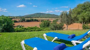 Dos sillones azules con toallas, un área con césped y vista a un paisaje montañoso con árboles y campos.