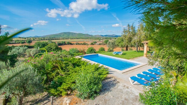 Piscina con sillones de descanso, rodeada de follaje y vistas a colinas distantes.
