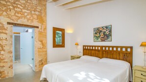 Un dormitorio con una cama grande, cabecera de madera, mesita de noche, lámpara de pared y una puerta que da a otra habitación.