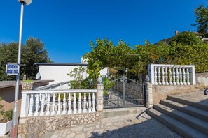 A stone staircase leading to a gated entrance with a white balustrade, a sign indicating 'APARTMENT FREE-FREE', and a clear blue sky in the background.
