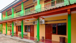 A two-story building with a balcony, potted plants, and a red tiled entrance.