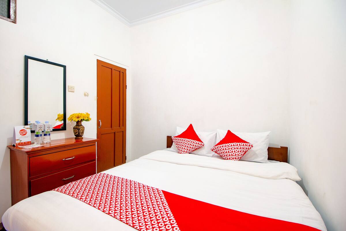 Une chambre d’hôtel avec un lit, une commode en bois, un miroir et une porte.