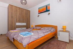 Une chambre à coucher comprenant un lit, une armoire en bois, une table de chevet avec une lampe et un tableau représentant un phare accroché au mur.