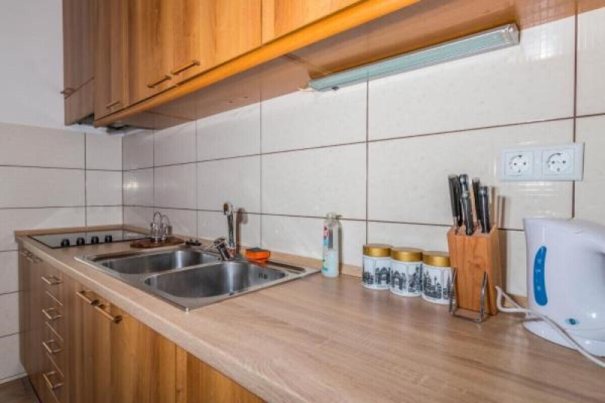 Une cuisine avec des meubles de rangement en bois, un évier à deux bacs et une bouilloire posée sur le plan de travail.