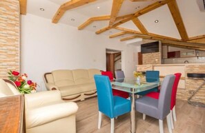 Un salon moderne avec une table à manger en verre, des chaises bleues et grises, un canapé beige et une structure de plafond en bois.
