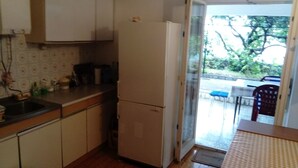 A compact kitchen with a refrigerator, sink, and a dining area with a table and chairs. - Apartment Neno (Crikvenica)