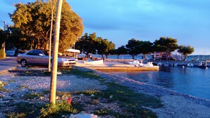 A waterfront area with a car parked near the shore, a boat dock, and a stone pathway leading to a seating area. - Apartment Neno (Crikvenica)