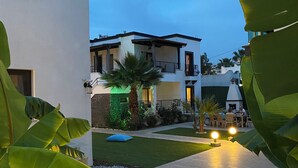 A modern building with a flat roof, large windows, and a balcony. There is a well-maintained lawn with a blue cushion and a fire extinguisher visible. - Orya Apart (Bodrum)