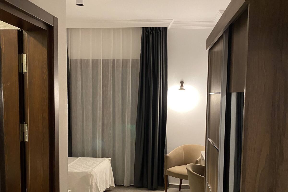 Une chambre d’hôtel avec un lit, une chaise, une armoire et un rideau.