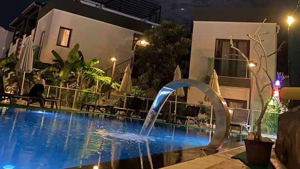 A nighttime pool area with a water feature, lounge chairs, and a moon in the sky. - Orya Apart (Bodrum)