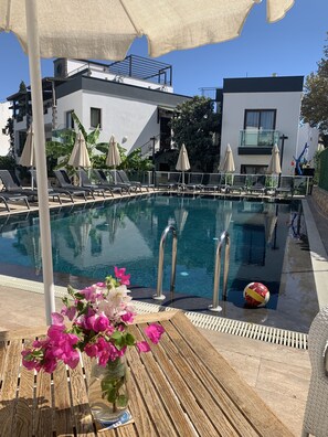 A pool area with lounge chairs, umbrellas, and a flower vase.