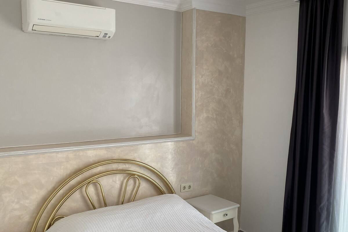 Une chambre d’hôtel équipée d’un lit, de tables de chevet, d’un appareil de climatisation et d’une fenêtre avec des rideaux.