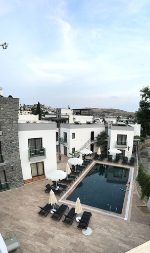 A rooftop pool area with lounge chairs and umbrellas, surrounded by modern buildings with a view of the cityscape.