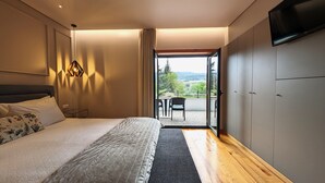 A modern bedroom with a large bed, a nightstand, a lamp, and a view of a balcony with outdoor furniture. - Quinta do Burgo (Amares)