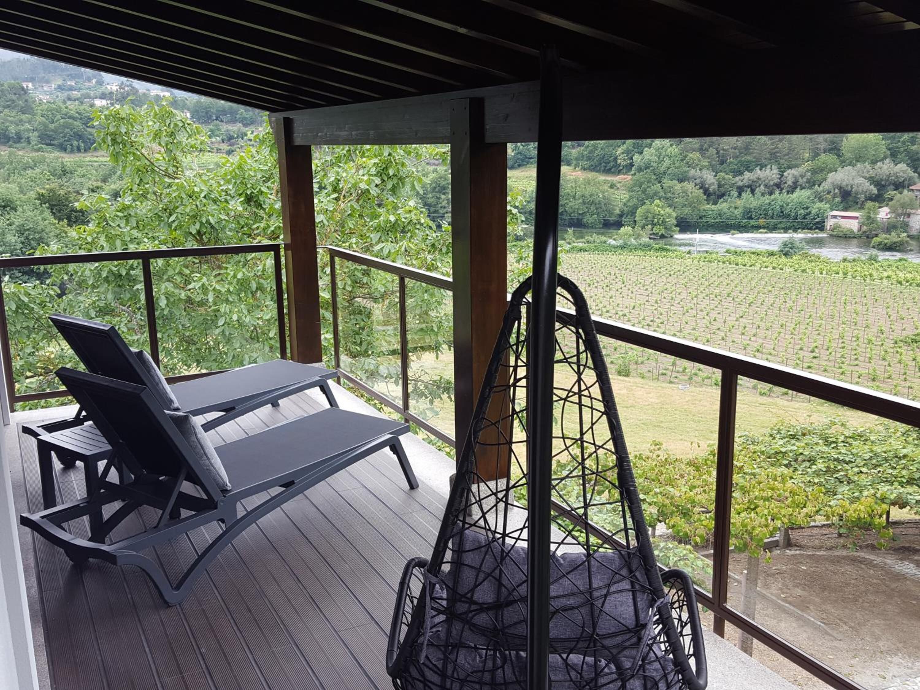 A balcony with a table and chairs, overlooking a vineyard.