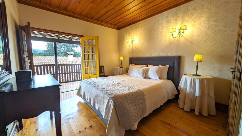 A bedroom with a bed, bedside tables, a desk, and a balcony with a wooden railing.