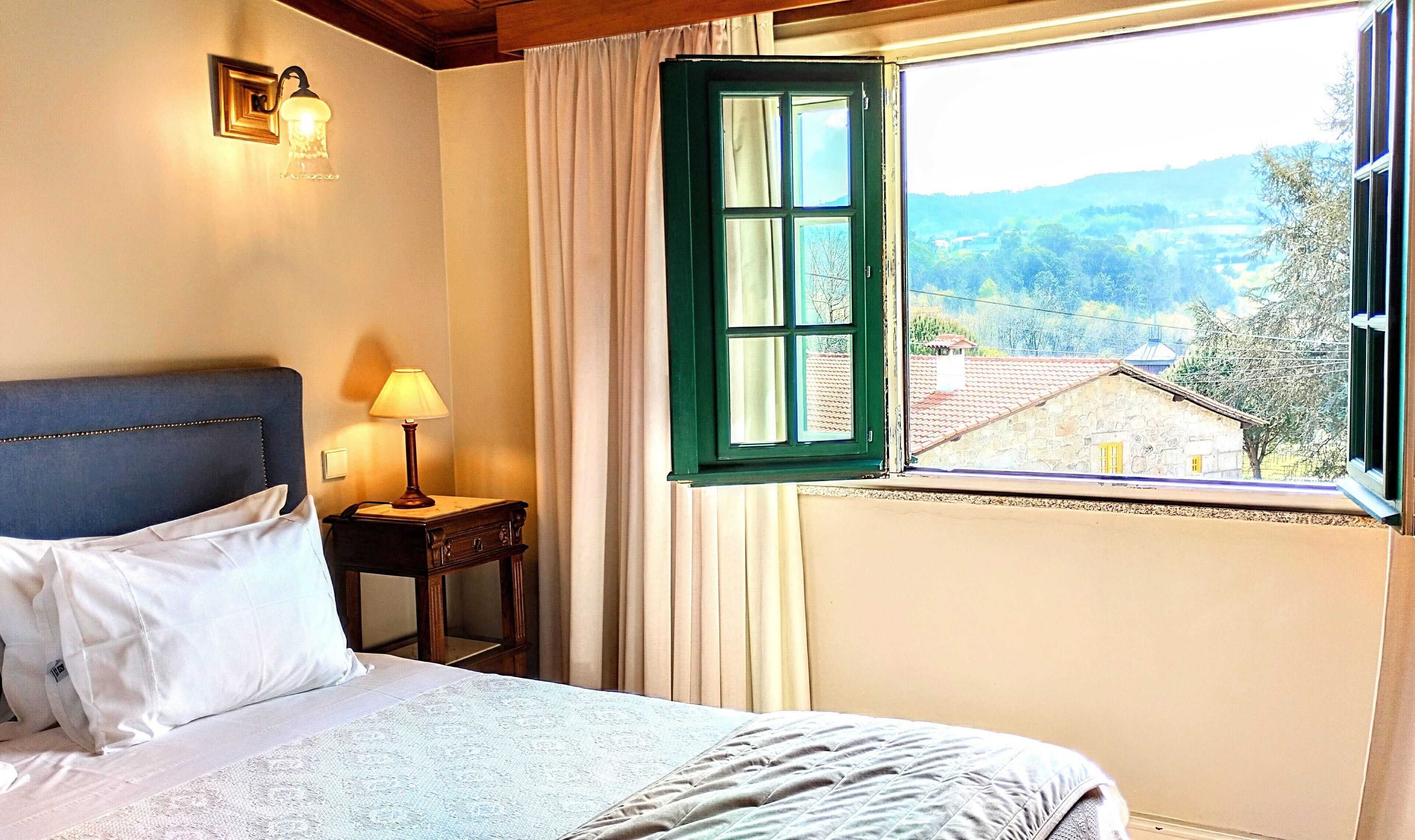 Un dormitorio con cama, mesita de noche con lámpara, y ventana con vistas al campo.