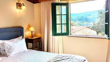 Un dormitorio con cama, mesita de noche con lámpara, y ventana con vistas al campo.