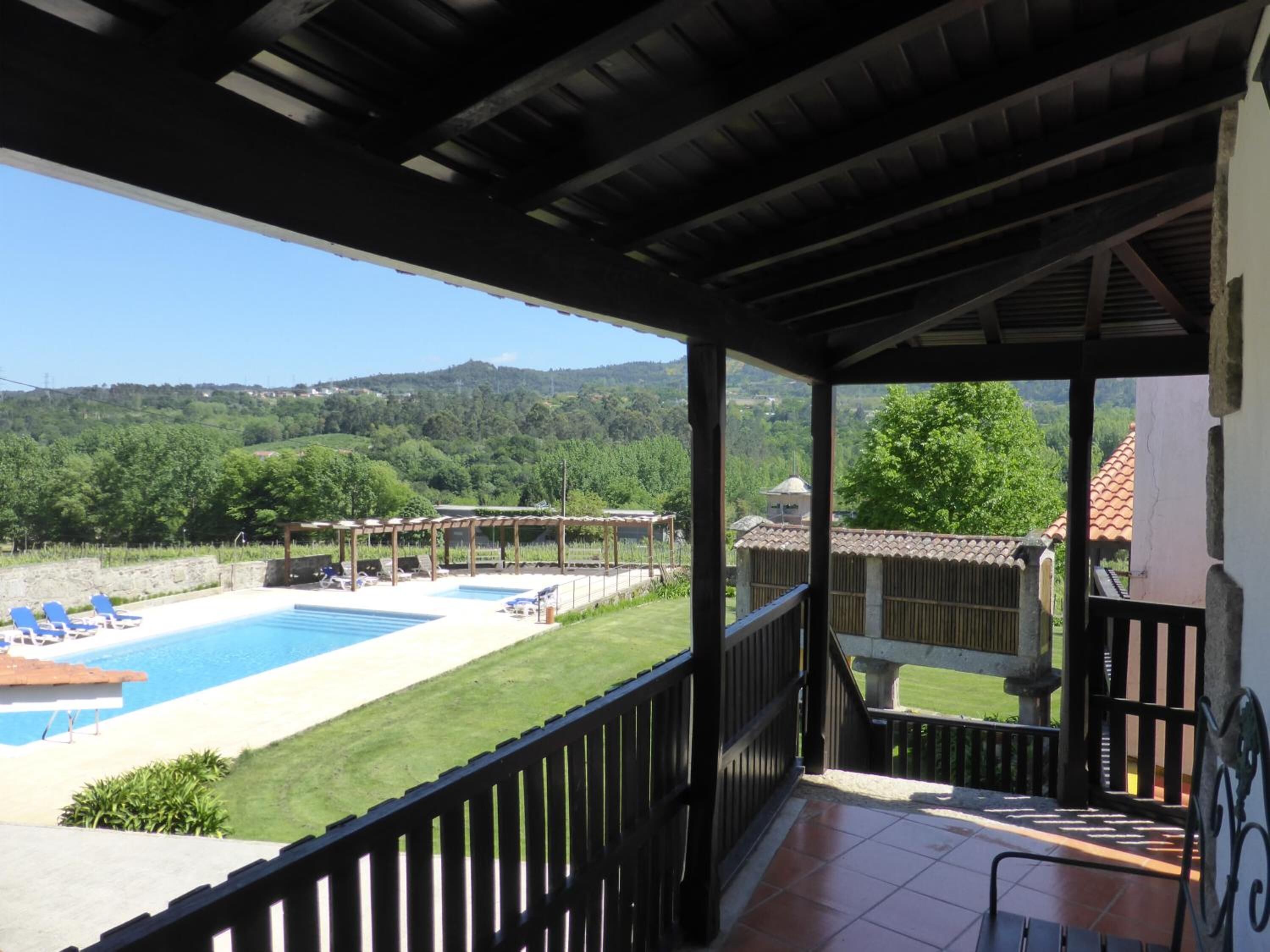 Ein überdachter Außenbereich mit Pool, Liegestühlen und Blick auf eine grüne Landschaft.