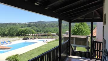 Ein überdachter Außenbereich mit Pool, Liegestühlen und Blick auf eine grüne Landschaft.